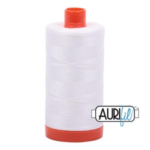 May include: A cylindrical spool of white sewing thread featuring a bright orange plastic cap at the top and an orange plastic base at the bottom. The brand name AURIfil is printed in black and blue text on the lower right side of the spool.