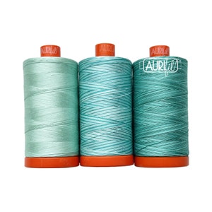 May include: Three spools of thread in shades of teal and light green. The spools are labeled "Aurifil" and have orange tops.