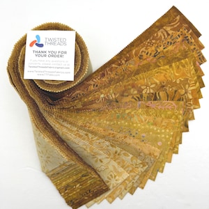 May include: A jelly roll of fabric strips featuring various shades of gold, tan, and brown with batik-style patterns. A white square card is tucked into the roll with the text TWISTED THREADS THANK YOU FOR YOUR ORDER and contact information.