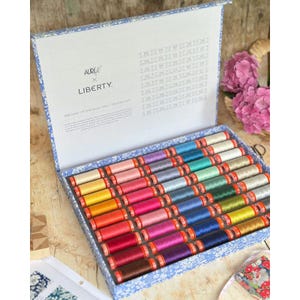May include: A box of Aurifil x Liberty thread spools in various colors. The box is open, revealing rows of colorful thread spools. The box has a blue floral pattern on the outside and the text "AURIFIL x LIBERTY" on the inside.