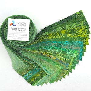 May include: A roll of green fabric strips with various shades and patterns, including floral and abstract designs. The fabric is fanned out, showcasing the different colors and textures. A small card with the text "TWISTED THREADS THANK YOU FOR YOUR ORDER!" is attached to the roll.