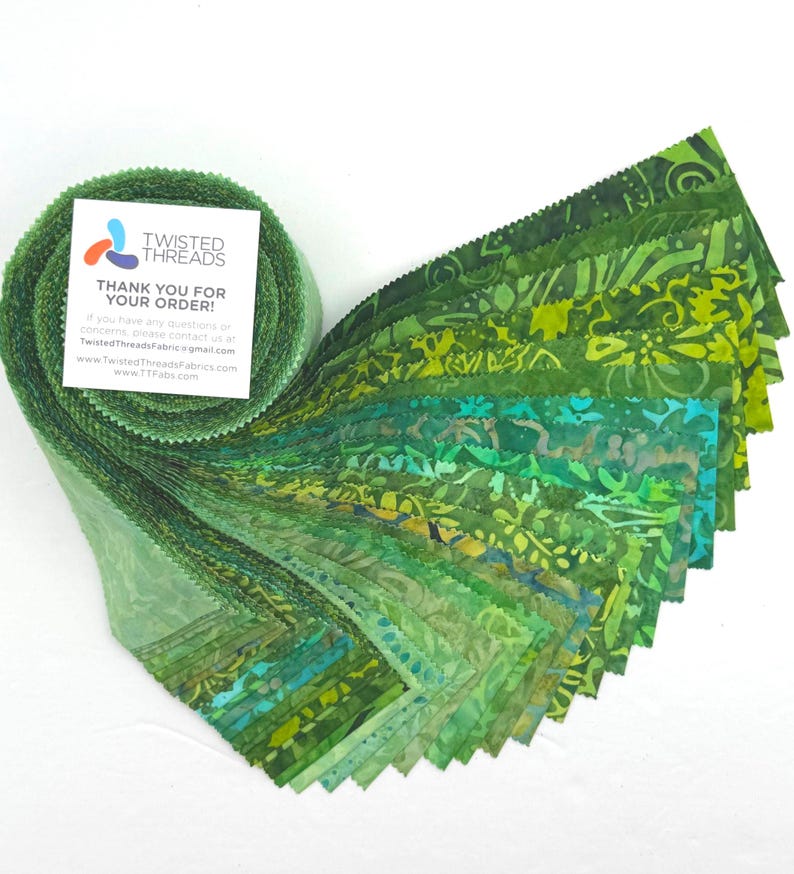 May include: A roll of green fabric strips with various shades and patterns, including floral and abstract designs. The fabric is fanned out, showcasing the different colors and textures. A small card with the text "TWISTED THREADS THANK YOU FOR YOUR ORDER!" is attached to the roll.