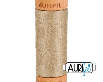 May include: A spool of light brown sewing thread wound around a wooden core. The top of the wooden spool is branded with the text AURIFIL, and the bottom is branded with the text MADE IN ITALY. A logo with the text AURIFIL is visible on the right.