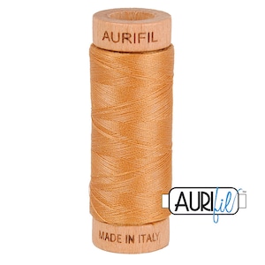 May include: A spool of Aurifil thread in a light orange color. The spool is made of wood and has the Aurifil logo and "Made in Italy" printed on it.