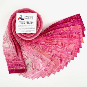 May include: A jelly roll of fabric strips in various shades of pink, featuring floral and abstract patterns. A square white card is tucked into the roll with the text TWISTED THREADS THANK YOU FOR YOUR ORDER! and contact information.