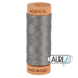 May include: A spool of dark gray sewing thread wound around a cylindrical wooden core. The top of the wooden spool is branded with the text AURIFIL, and the bottom is branded with the text MADE IN ITALY. The thread has a smooth texture.