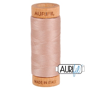 May include: A spool of Aurifil thread in a light peach color. The thread is wound around a wooden spool with the Aurifil logo and "MADE IN ITALY" printed on the spool. The thread is tightly wound and ready for use.