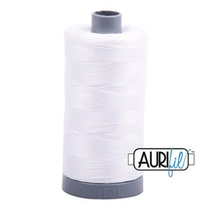 May include: A spool of white sewing thread wound onto a cylindrical core with grey plastic ends. The brand name Aurifil is embossed on the bottom base and printed in black and blue text on a white rectangular label attached to the side.