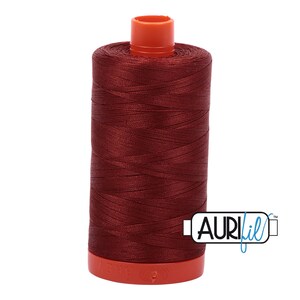 May include: A spool of maroon colored thread with an orange plastic bobbin and the text "Aurifil" in blue.