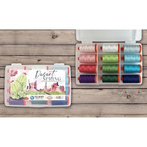 May include: A set of twelve spools of thread in a clear plastic storage case. The label features a desert landscape illustration with the text Desert Spring, Island Batik, and Aurifil. The spools are arranged in three columns of four colors.