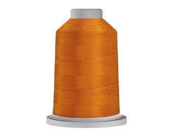 Puede incluir: Un carrete de hilo de bordar de color naranja vibrante con un acabado suave y lustroso. El hilo está enrollado firmemente alrededor de un núcleo cilíndrico con una base y una tapa de plástico gris claro, creando un aspecto uniforme.