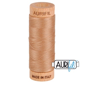 May include: A spool of Aurifil thread in a light brown color. The spool is made of wood and has the Aurifil logo printed on it. The spool is labeled "Made in Italy".