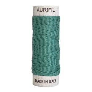 May include: A spool of teal thread wrapped around a cylindrical wooden core. The top of the spool features the text AURIFIL printed in black, while the bottom of the spool features the text MADE IN ITALY printed in black.