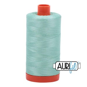 May include: A spool of light mint green sewing thread featuring a bright orange plastic top and base. The spool is wrapped in smooth, tightly wound thread and includes a white rectangular logo with the black text AURIfil on the bottom right.