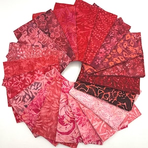 May include: A circular arrangement of fabric swatches in various shades of red and pink. Each piece features distinct batik-style patterns, including floral motifs, dots, and abstract shapes, creating a gradient from deep crimson to light rose.