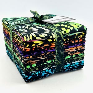 May include: A stack of folded fabric squares featuring a black background with vibrant, multi-colored batik patterns in shades of yellow, orange, purple, green, and blue. The stack is secured with a matching fabric ribbon and a small white label.