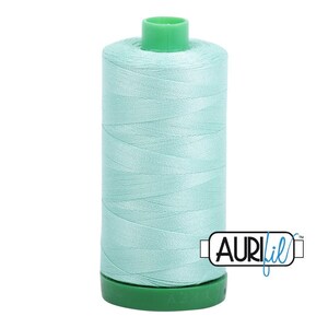 May include: A spool of light mint green sewing thread featuring a cylindrical shape with a green plastic top and base. The brand name AuriFil is printed in black and blue text on a white rectangular label attached to the lower right side.