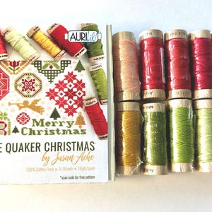 May include: A collection of colorful embroidery floss spools and a booklet titled "Little Quaker Christmas by Susan Ache." The floss includes shades of red, green, yellow, and peach. The booklet features cross-stitch patterns with Christmas themes.