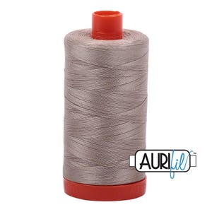 May include: A spool of light taupe sewing thread featuring a bright orange plastic top and base. The spool is wrapped in smooth, tightly wound thread and displays the brand name AuriFil in a black and blue logo on the lower right side.
