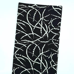 May include: A rectangular piece of fabric featuring a black background with a repeating white pattern of curved, dotted lines that intersect and overlap across the surface, creating a continuous abstract design throughout the entire material.