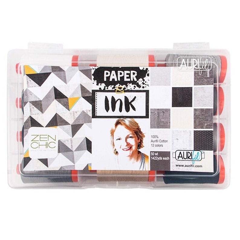 Op de afbeelding: Een transparante kunststof opbergdoos met 12 spoelen Aurifil garen. De spoelen zijn zwart en grijs en hebben een rood label met de tekst "Paper & Ink". De doos heeft ook een label met de tekst "Zen Chic" en een foto van een vrouw. Het label zegt ook "100% Aurifil Cotton, 12 kleuren, 50 wt, 1422yds each".