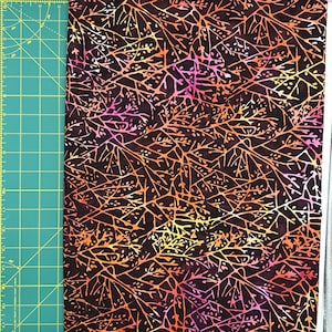 May include: A piece of fabric with a dark brown background and a colorful, branching pattern in shades of orange, yellow, and pink. The fabric is next to a green cutting mat with white measurement markings.