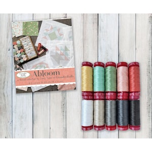 May include: A collection of twelve spools of thread in various colors including yellow, green, pink, red, white, beige, and gray, alongside a product card titled Abloom by Corey Yoder of Coriander Quilts featuring quilt block patterns.