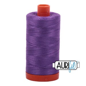 May include: A spool of vibrant purple sewing thread wound onto a cylindrical plastic core. The spool features a bright orange top and bottom cap, with the brand name AURIfil printed in black and blue text on a white rectangular label.