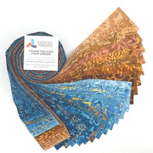 May include: A bundle of fabric strips in shades of blue, brown, and gold, with floral and abstract patterns. The fabric is arranged in a fan shape, with a card that reads "THANK YOU FOR YOUR ORDER!" from Twisted Threads.