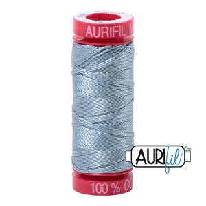 May include: A spool of light blue sewing thread wrapped around a red plastic core. The top and bottom of the red spool feature white text that reads Aurifil, 100% Cotton, and other markings. A logo with the text Aurifil is visible on the right side.