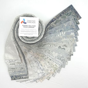 May include: A jelly roll of fabric strips featuring various shades of gray, blue, and white with diverse patterns including dots, florals, and abstract shapes. A square white card with the text TWISTED THREADS THANK YOU FOR YOUR ORDER is included.