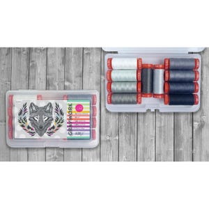 May include: A clear plastic storage case containing ten small spools of cotton thread in shades of white, gray, and black. The lid features a graphic of a wolf head surrounded by colorful leaves and the text Aurifil Gray Work 50 wt.