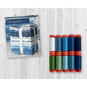 May include: A stack of blue and white patterned fabric squares labeled Blueprint by Camille Roskelley and a set of ten spools of Aurifil 100% cotton thread in shades of blue, green, and white, each spool featuring a red cap and base.