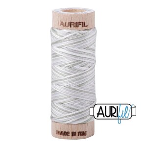 May include: A spool of light gray and white variegated thread wound around a cylindrical wooden core. The top of the wooden spool is branded with the text AURIFIL, and the bottom base features the text MADE IN ITALY in a dark brown font.
