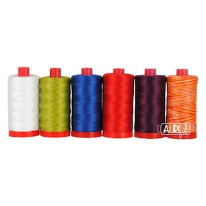 May include: Six cylindrical spools of thread arranged in a row, featuring colors of white, olive green, royal blue, bright red, deep purple, and an orange-and-yellow variegated pattern. Each spool has a red plastic base and the Aurifil logo.