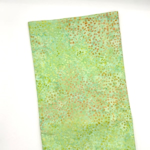 May include: A rectangular piece of fabric with a green and yellow mottled pattern, accented with small orange-brown spots. The fabric has a watercolor-like appearance, with a light, airy feel. The background is white.