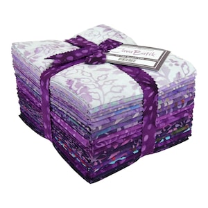 May include: A stack of batik fabric squares in shades of purple, lavender, and white, tied with a purple ribbon. The fabric has floral and abstract patterns. A tag reads "Java Batik".