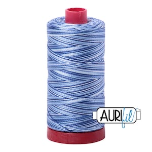 May include: A spool of blue and white variegated thread with a red plastic top and bottom. The thread is labeled "Aurifil" in blue lettering.