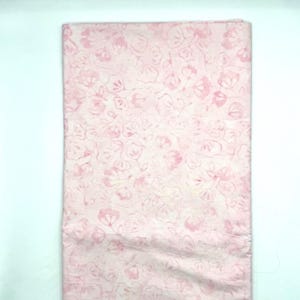 May include: A folded piece of fabric with a delicate floral pattern in shades of pink. The design features small, stylized flowers and leaves scattered across a light pink background. The fabric appears to be soft and lightweight.