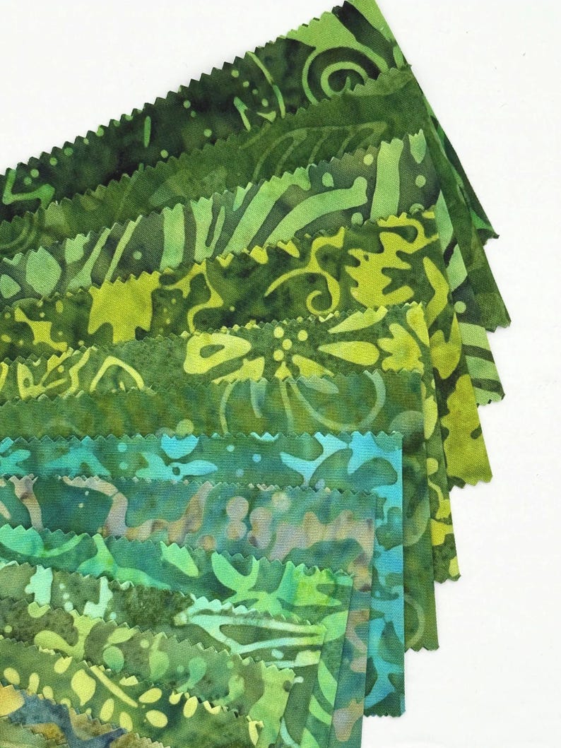May include: A collection of green fabric swatches with various patterns and shades, ranging from dark forest green to bright lime. The edges of the fabric are cut with a decorative, zigzag pattern. The fabrics have a batik-like appearance.