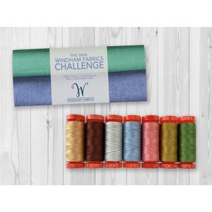 May include: A set of seven small spools of 50wt cotton thread in various colors, including gold, brown, silver, light blue, pink, mustard, and green, with red caps, accompanied by a label reading The 2026 Windham Fabrics Challenge.