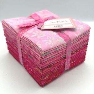 May include: A stack of folded fabric squares in various shades of pink, ranging from light to dark, tied with a pink ribbon. A rectangular tag on top features the text Java Batik and 20 Fat Quarters, with a barcode visible at the bottom.