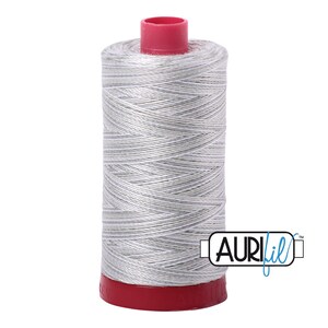 May include: A spool of silver gray thread with a red plastic top and bottom. The spool is labeled "Aurifil" in blue.