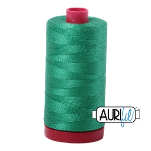 May include: A spool of green thread with a red top and bottom. The spool is labeled "Aurifil" in blue.