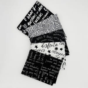 May include: A stack of fabric squares in black and white, each printed with inspirational words and phrases. The fabrics feature text like "imagine," "curious," and "disfruta," with floral and star accents.