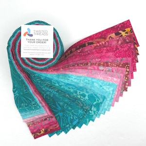 May include: A stack of fabric strips in shades of teal, pink, and magenta, with a floral pattern. The fabric is fanned out, revealing the different colors and designs. A small white card with text is attached to the fabric.