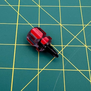 May include: A small, red and clear handled screwdriver with a black tip. The handle is a hexagonal shape with red accents. The screwdriver is designed for precision work.