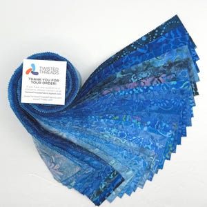 May include: A jelly roll of fabric strips in various shades of blue, featuring batik-style patterns. A white square card is attached to the roll, displaying the text TWISTED THREADS, THANK YOU FOR YOUR ORDER, and contact information for TwistedThreadsFabric.