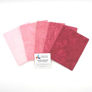 May include: Five rectangular fabric swatches arranged in a fan shape, transitioning in color from pale baby pink to deep magenta. Each piece features a mottled batik-style texture. A small white square card with the text Twisted Threads is included.