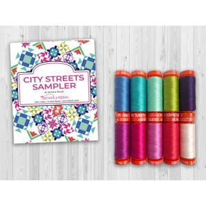 May include: A City Streets Sampler quilt pattern booklet by Jemima Flendt and a set of ten small spools of 50wt 100% cotton thread in various colors including blue, teal, green, purple, pink, magenta, and white with orange spool caps.